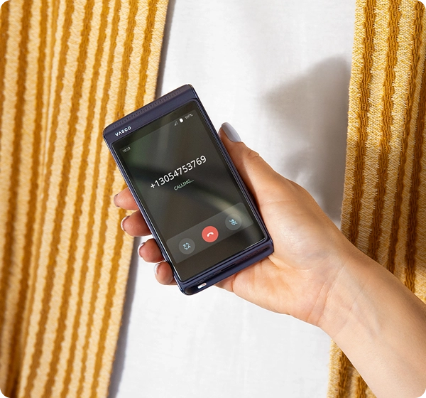 A person holding the Vasco Translator Q1. The screen displays the calling feature with a phone number, the 