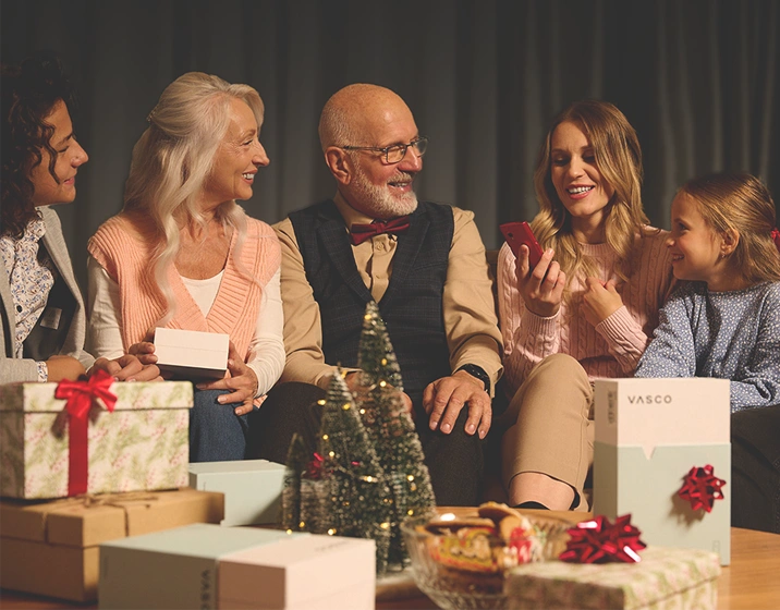 A smiling family sits together surrounded by gifts. One person holds a translator.