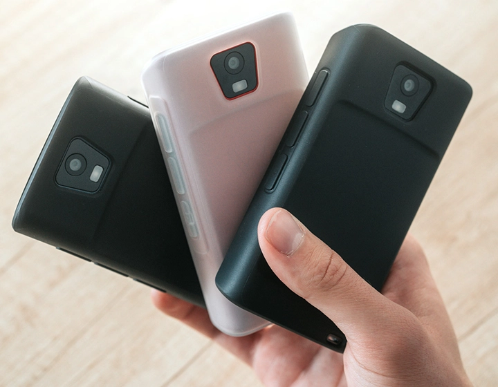 Person holding three Vasco Translator Q1 devices in silicone cases, presenting three different case colors: Solid Black, Dark Caramel, and Milky White.