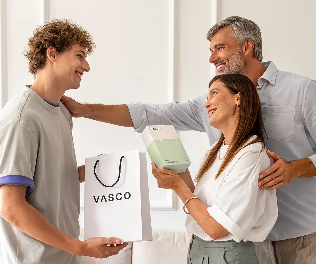A heartwarming scene of three people smiling and standing together. On the left, a young man with curly hair holds a white 